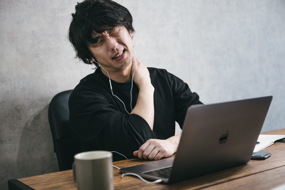 デスクワーク中に首すじを押さえる男性のイメージ